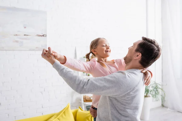 Hombre sosteniendo alegre hija y bailando en casa - foto de stock