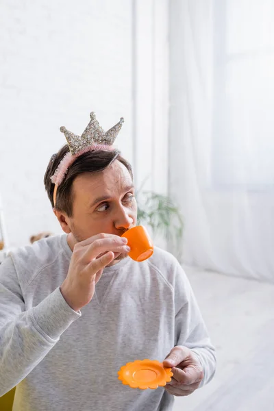 Adulto hombre jugando príncipe y beber de juguete taza en casa - foto de stock