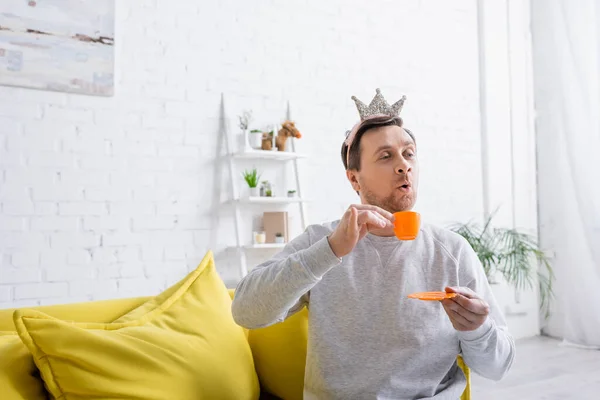 Homem alegre usando coroa de brinquedo enquanto joga príncipe em casa — Fotografia de Stock