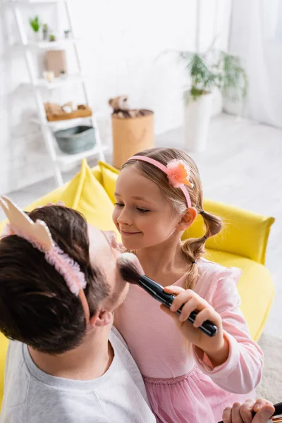 High angle view of smiling girl doing makeup to father in toy crown — Stock Photo