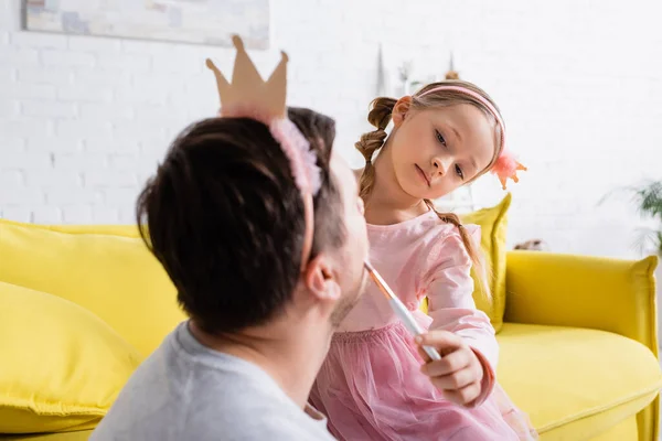 Child in toy crown doing visage to father on blurred foreground — Stock Photo