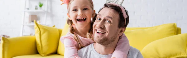 Riendo papá y hija en coronas de juguete mirando a la cámara, bandera - foto de stock