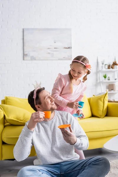 Happy dad and daughter looking at each other while holding toy cups in living room — Stock Photo