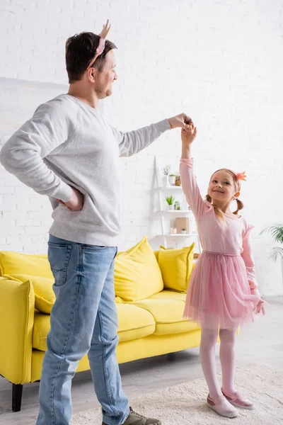 Adult man in toy crown holding hand on hip while dancing with daughter — Stock Photo