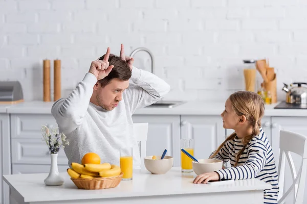 Hombre mostrando el gesto cuerno de toro mientras se divierten durante el desayuno con su hija - foto de stock