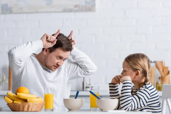 Pai mostrando chifres de touro gesto perto da filha durante o café da manhã — Fotografia de Stock