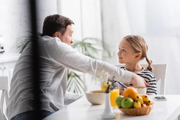 Усміхнена дівчина дивиться на батька під час сніданку на кухні, розмитий передній план — стокове фото