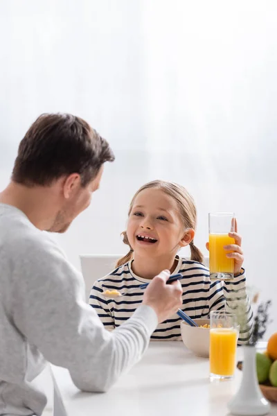Aufgeregtes Kind hält Glas Orangensaft neben Vater im verschwommenen Vordergrund — Stockfoto