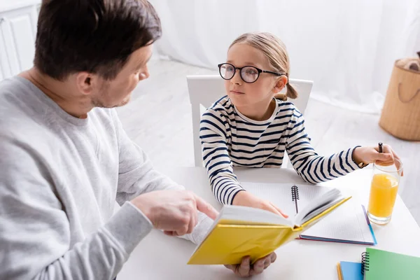Girl pointing with finger at notebook near daughter doing homework in kitchen — Stock Photo