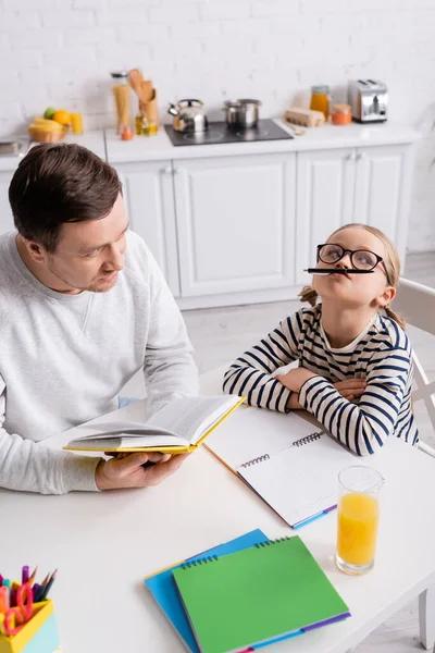 Man holding textbook near playful daughter with pen near nose — Stock Photo