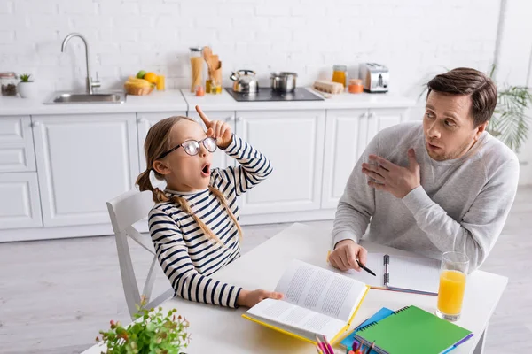 Excité enfant montrant geste idée tout en faisant des devoirs près de père étonné — Photo de stock