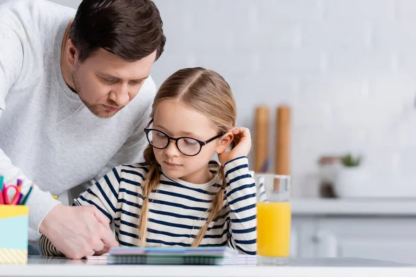 Pai ajudando filha fazendo lição de casa na cozinha, foreground borrado — Fotografia de Stock
