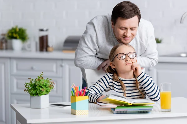 Padre sorridente vicino figlia premurosa facendo i compiti in cucina — Foto stock
