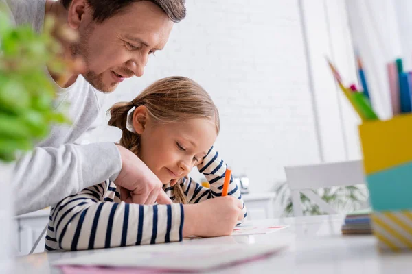 Father pointing with finger near concentrated daughter drawing with felt pen on blurred foreground — Stock Photo