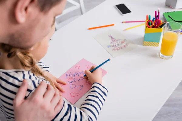 Vue partielle de l'enfant dessinant la carte heureuse de jour de femmes près du père sur le premier plan flou — Photo de stock