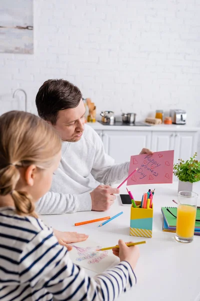 Homme pointant avec stylo à la carte heureuse de jour de femmes près de fille dessin sur le premier plan flou — Photo de stock