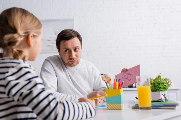 Hombre sosteniendo feliz mujer días tarjeta cerca de hija en primer plano borrosa - foto de stock