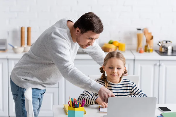 Man pointing at laptop near daughter during online lesson at home — Stock Photo