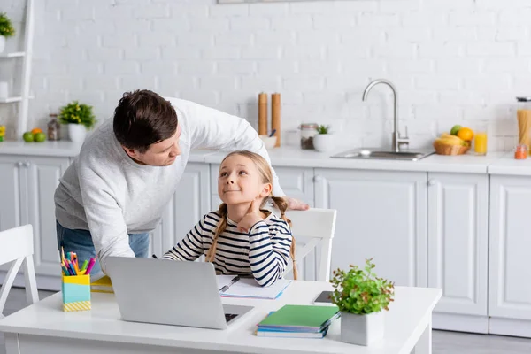 Отец и дочь смотрят друг на друга во время онлайн урока на кухне — стоковое фото