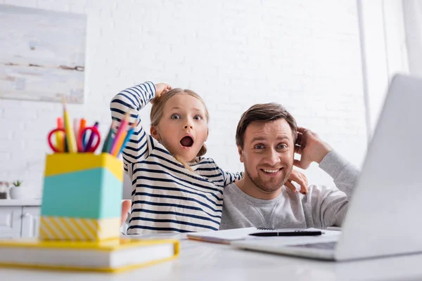 Excited father and daughter touching heads during online lesson at home, blurred foreground — Stock Photo