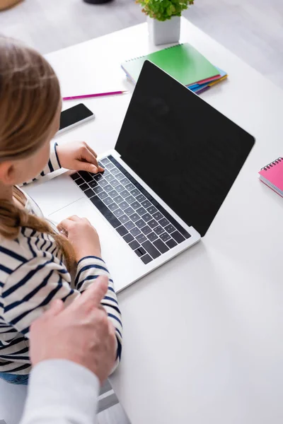 Vista ritagliata della studentessa vicino al computer portatile con schermo bianco e padre a casa — Foto stock