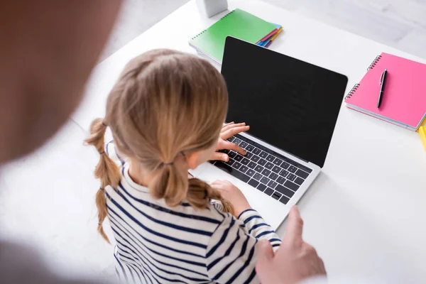 Visão de alto ângulo da menina perto de laptop e pai apontando com o dedo em primeiro plano desfocado — Fotografia de Stock