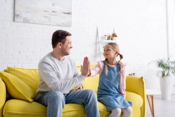 Feliz niño dando alta cinco a padre en sofá en casa - foto de stock