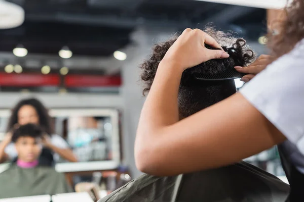 Coiffeur afro-américain peigner les cheveux du client en cape — Photo de stock