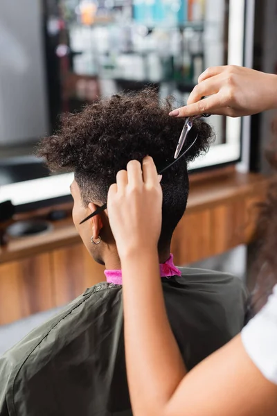 African american hairdresser with comb haircutting client — Stock Photo