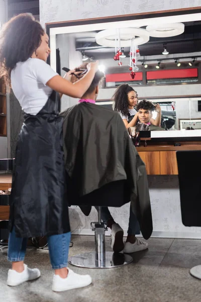 Parrucchiere afroamericano che taglia i capelli del cliente in primo piano sfocato nel salone — Foto stock