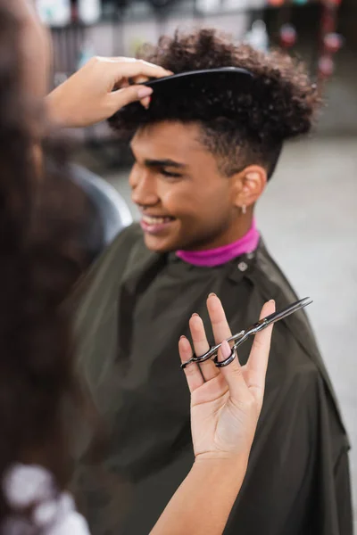 Ножницы в руке африканского американского парикмахера расчесывания клиента на размытом фоне — стоковое фото