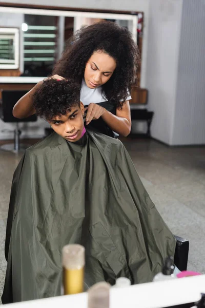 Peluquería afroamericana recortando cuello de cliente en capa en salón - foto de stock