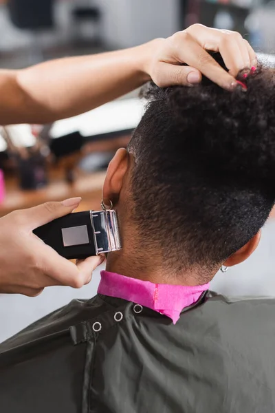 Hairdresser trimming neck of african american client in cape and collar paper — Stock Photo