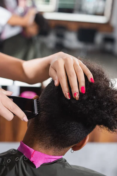 Hairdresser trimming hair of african american man in salon — Stock Photo