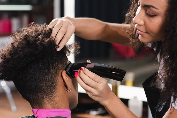 African american hairdresser trimming hair of young man — Stock Photo