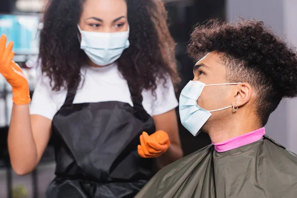 Cliente afro-americano em máscara médica olhando para cabeleireiro em fundo borrado — Fotografia de Stock