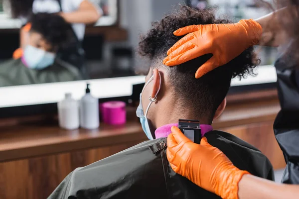Африканский американский парикмахер стрижет шею мужчине в медицинской маске — стоковое фото