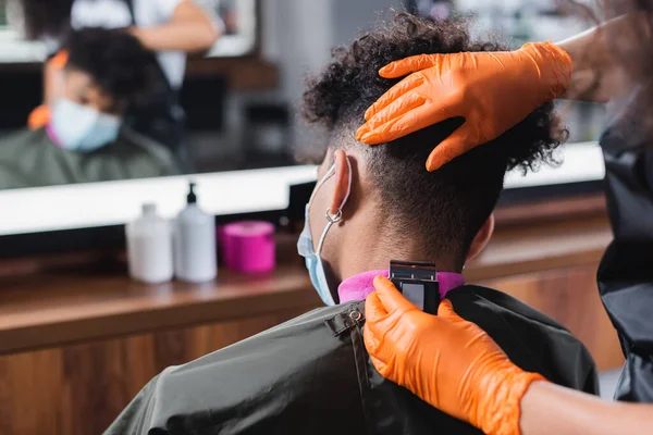 African american hairdresser trimming neck of man in medical mask — Stock Photo