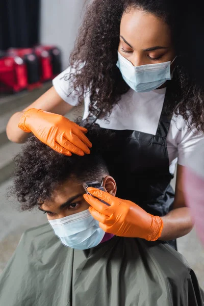 Coiffeur afro-américain dans le masque de protection coupe les cheveux de l'homme pendant la coupe de cheveux — Photo de stock