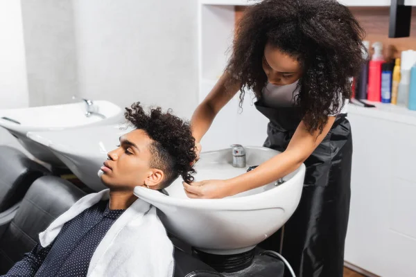 African american hairstylist washing hair of man in towel — Stock Photo