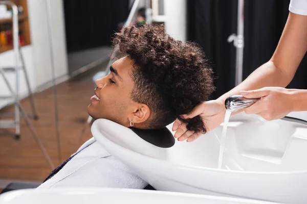 Sorridente cliente africano americano seduto vicino parrucchiere con doccia — Foto stock