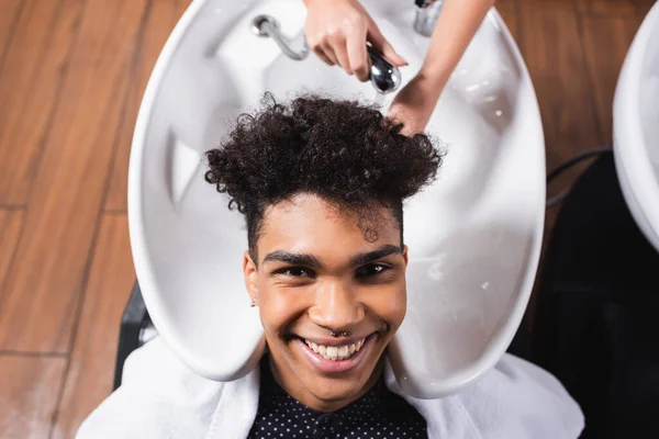 Vue du dessus du client afro-américain souriant assis près du coiffeur avec douche — Photo de stock