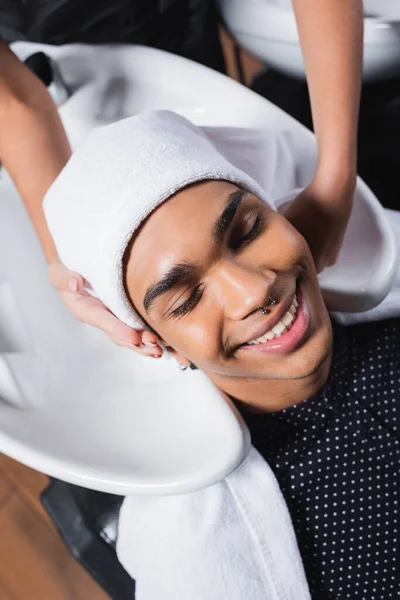 Vista dall'alto del cliente afroamericano sorridente seduto vicino al lavandino e parrucchiere con asciugamano — Foto stock