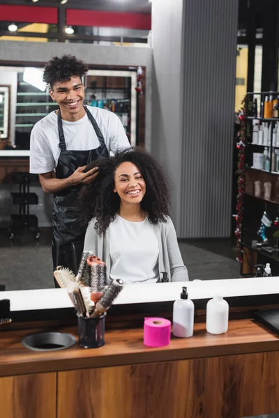 Smiling african american woman sitting near hairstylist in salon — Stock Photo