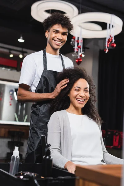 Позитивный африканский клиент и парикмахер улыбаются перед камерой в салоне — стоковое фото