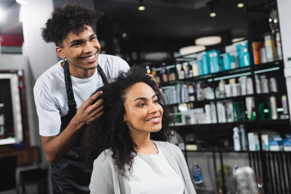 Sonriente peluquero afroamericano de pie cerca de una joven - foto de stock