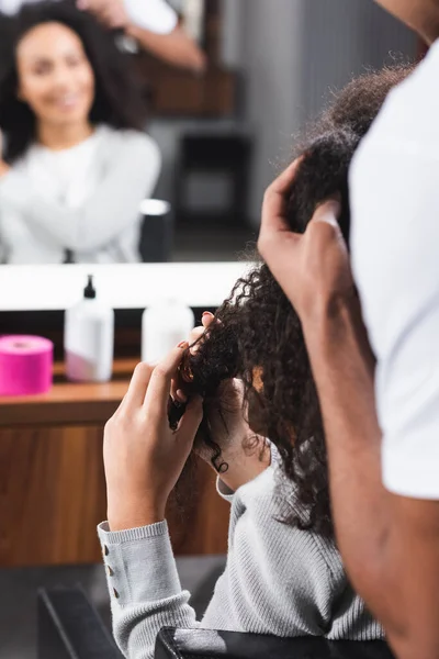 Coiffeur afro-américain au premier plan flou touchant les cheveux bouclés du client — Photo de stock