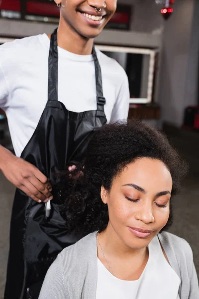 Afroamerikanerin sitzt neben lächelndem Friseur auf verschwommenem Hintergrund — Stockfoto