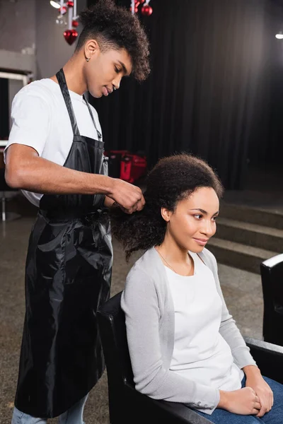 Peluquería afroamericana tejiendo pelo de cliente en salón - foto de stock