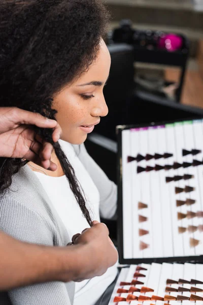 Hairstylist holding hair of african american client with color swatches — Stock Photo
